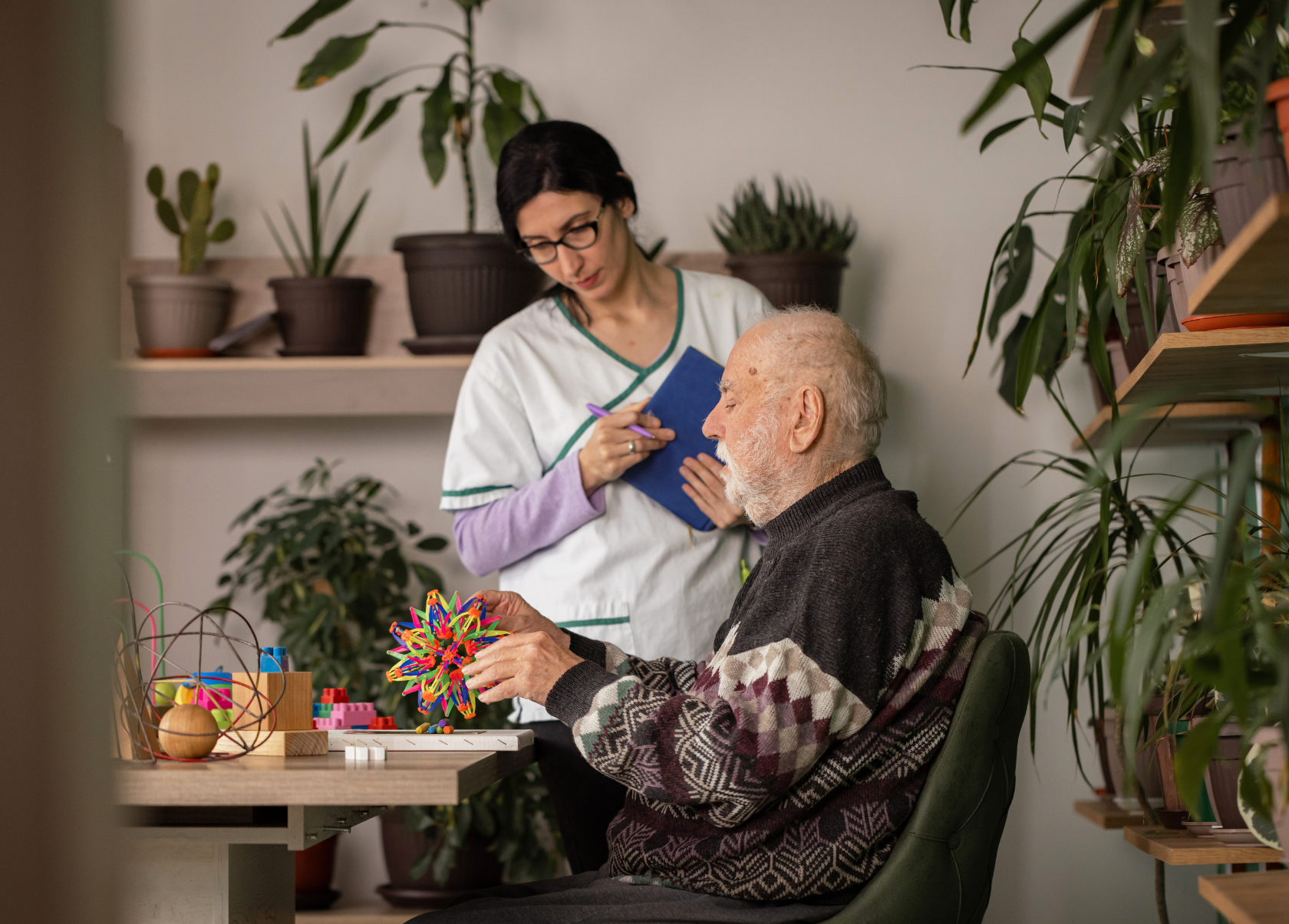 Caretaker standing with a senior man sitting at a table, doing brain exercises