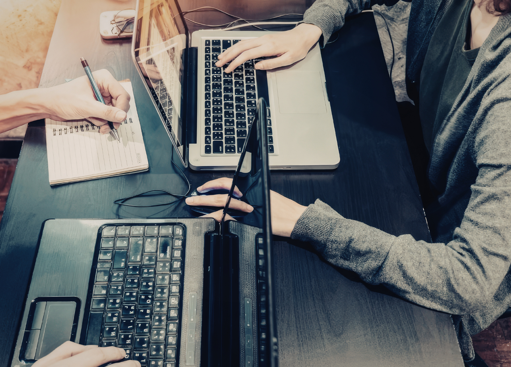 Close-up of 2 people working across a table from each other, each with a laptop in front of them