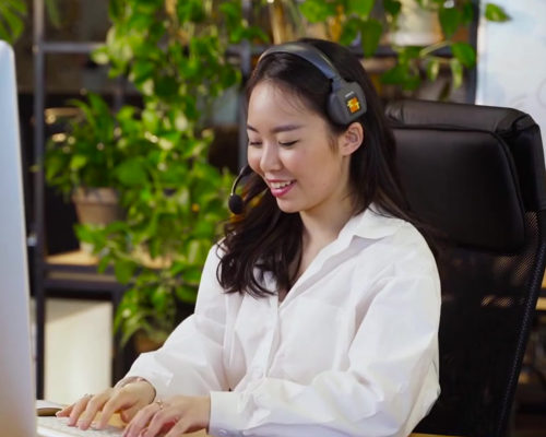 Woman wearing headset, sitting at a desk in front of a computer